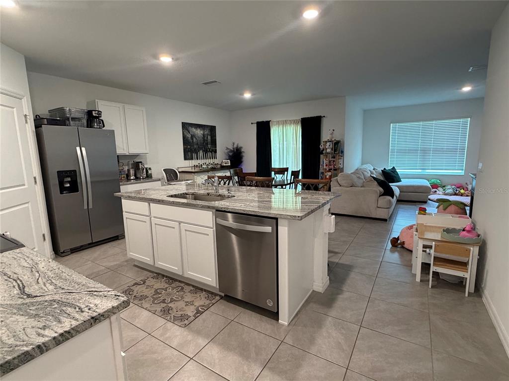 A kitchen with a granite-topped island and stainless steel appliances opens to a living area — 10866 QUAIL GROVE WAY, SAN ANTONIO, FL