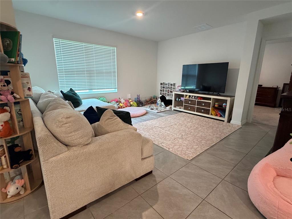 A living room features a beige sofa, a television on a media console, and tile flooring — 10866 QUAIL GROVE WAY, SAN ANTONIO, FL