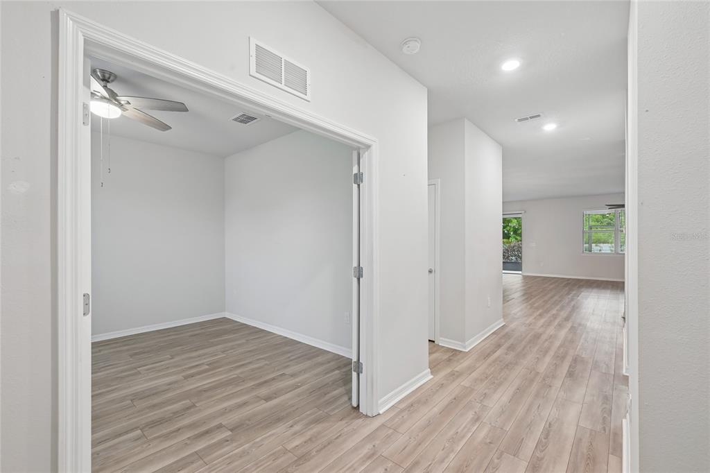 A room with a ceiling fan and light-colored wood flooring opens into a hallway — 11716 BRIGHTON KNOLL LOOP, RIVERVIEW, FL