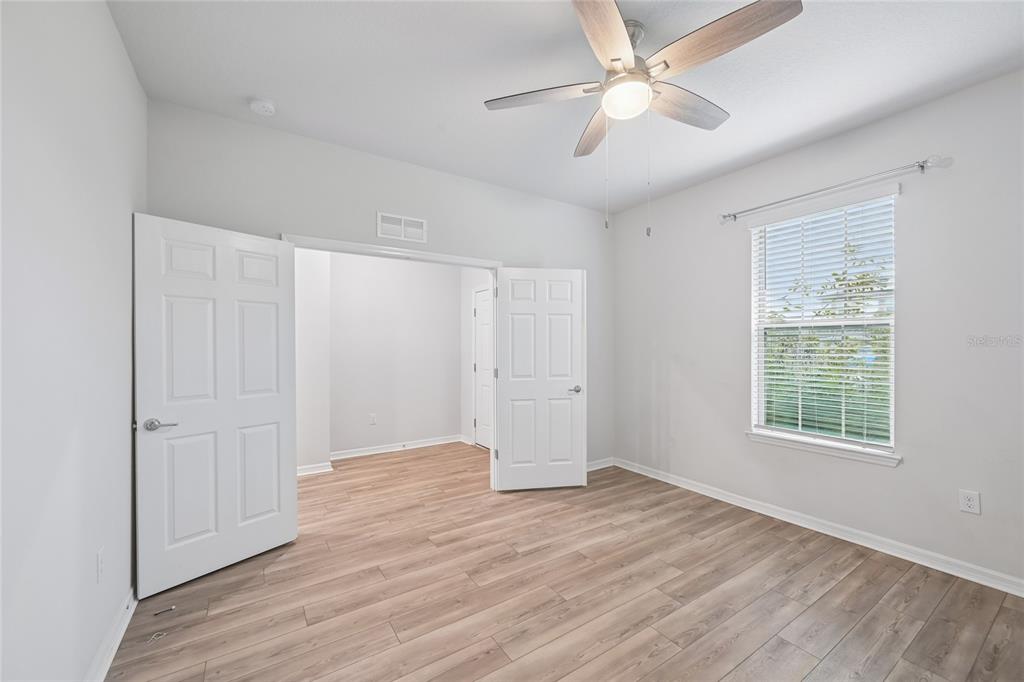 A bedroom with light wood-look flooring, white walls, a ceiling fan, and double doors — 11716 BRIGHTON KNOLL LOOP, RIVERVIEW, FL