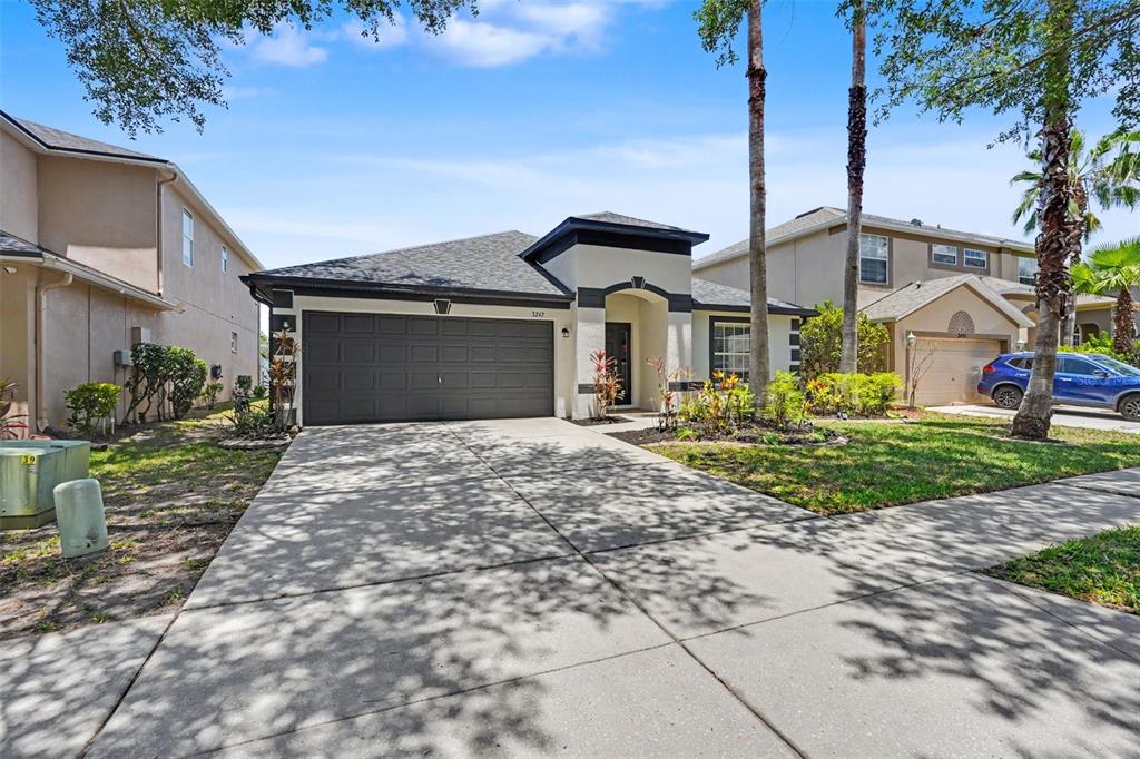A single-story house with a dark garage door, beige stucco walls, and a concrete driveway — 3247 DUNSTABLE DRIVE, LAND O LAKES, FL