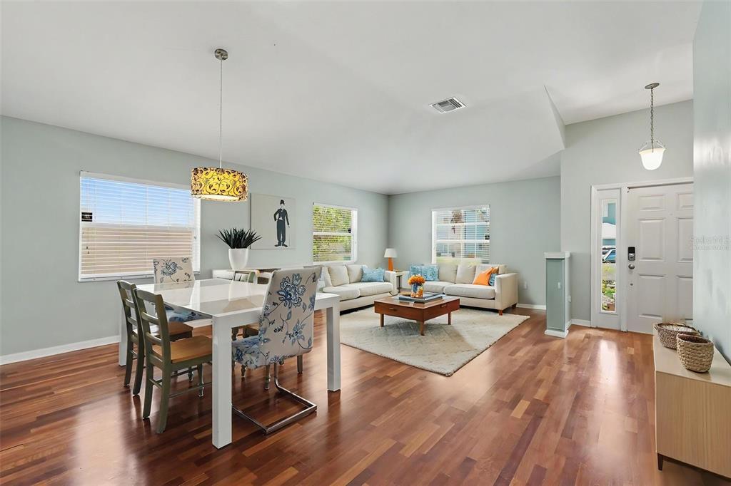 An open-concept living and dining area features hardwood floors, a vaulted ceiling, and neutral walls — 3247 DUNSTABLE DRIVE, LAND O LAKES, FL