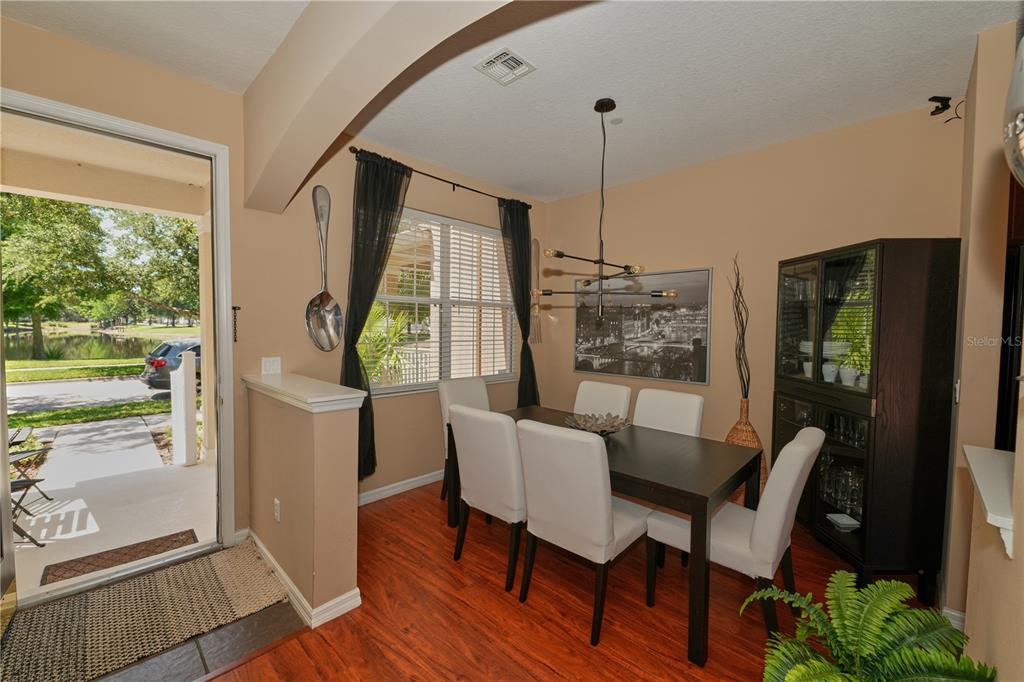 A dining room features a dark wood table, white chairs, and a view of a pond — 9135 CARDINAL MEADOW TRAIL, ORLANDO, FL