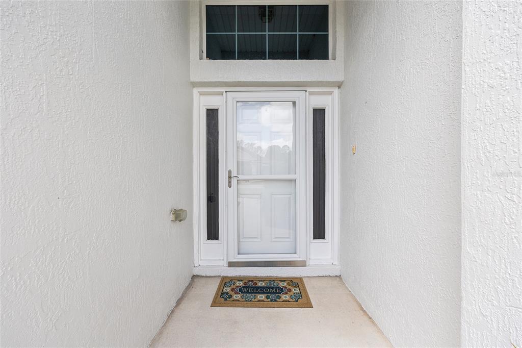 A white front door with a storm door and transom window sits in a recessed entryway — 11719 SW 72ND CIRCLE, OCALA, FL