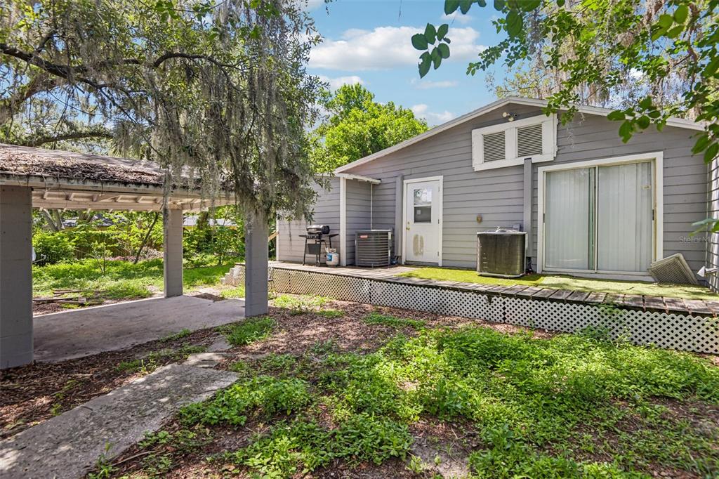The exterior of a gray house features a wooden deck, a carport, and landscaping — 1504 E 99TH AVENUE, TAMPA, FL