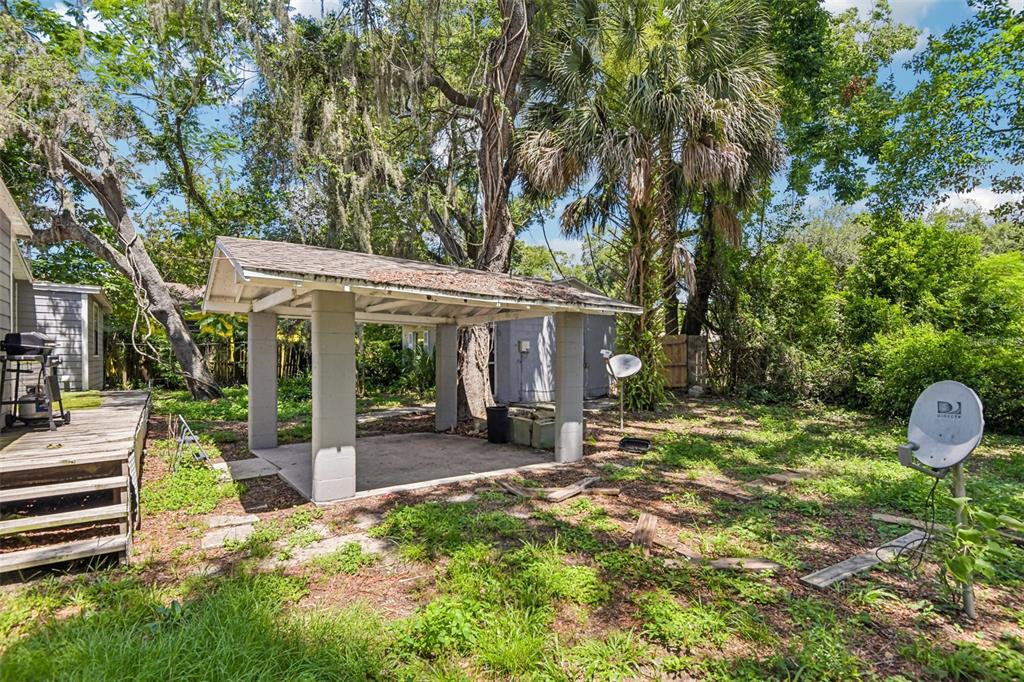 A backyard features a concrete patio with a covered roof, a wooden deck, and trees — 1504 E 99TH AVENUE, TAMPA, FL