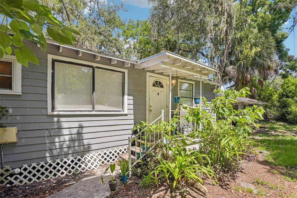 A gray wood-sided house features a small front porch with a white door and lattice — 1504 E 99TH AVENUE, TAMPA, FL