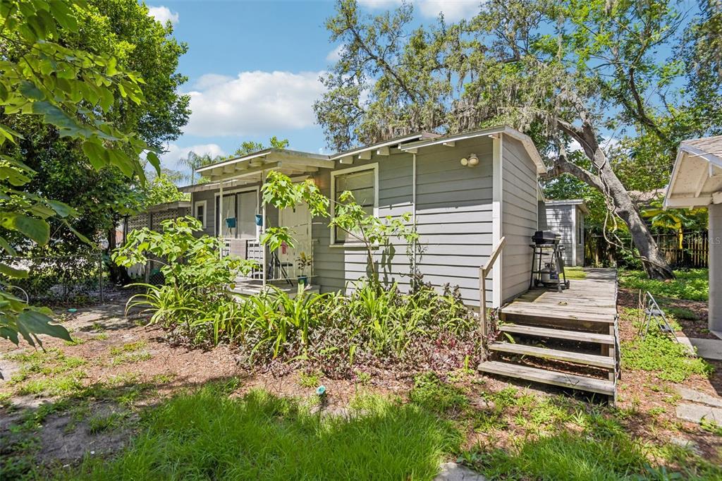A gray, single-story house with a wooden deck and stairs sits in a grassy yard — 1504 E 99TH AVENUE, TAMPA, FL