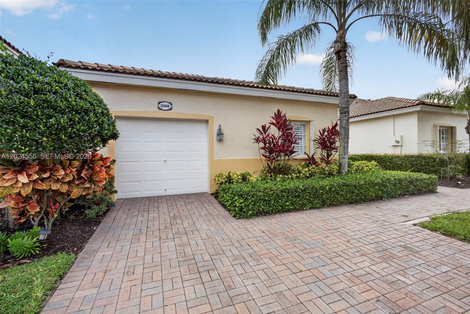 A single-story house features a white garage door, a brick driveway, and tropical landscaping — 2368 Windjammer Way, West Palm Beach FL 33411, WEST PALM BEACH, FL