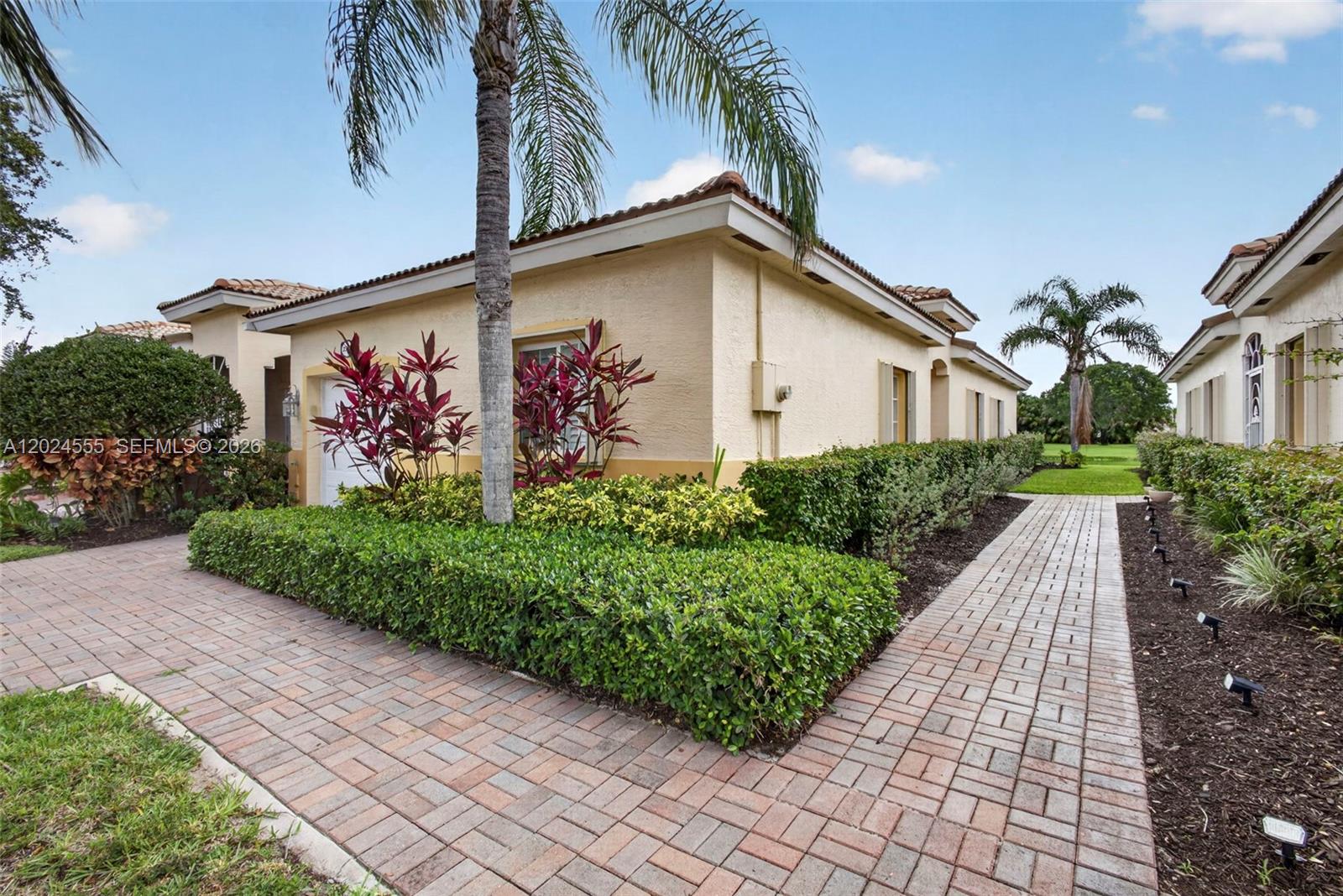A paved walkway leads past a tan house with a palm tree and manicured hedges — 2368 Windjammer Way, West Palm Beach FL 33411, WEST PALM BEACH, FL