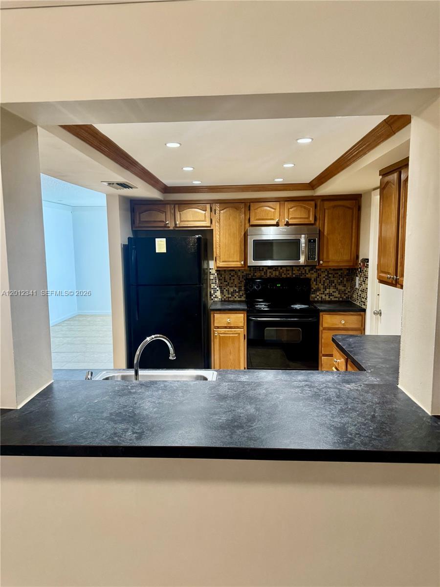 A kitchen features wood cabinets, black appliances, and a dark countertop with a breakfast bar — 1010 NW 72nd Ter # 0, Margate FL 33063, MARGATE, FL