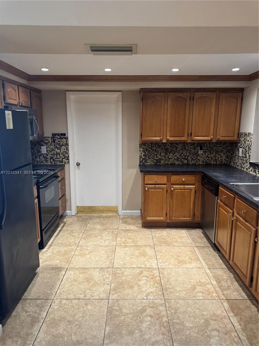 A kitchen features wood cabinets, dark countertops, a black refrigerator, and tiled flooring — 1010 NW 72nd Ter # 0, Margate FL 33063, MARGATE, FL
