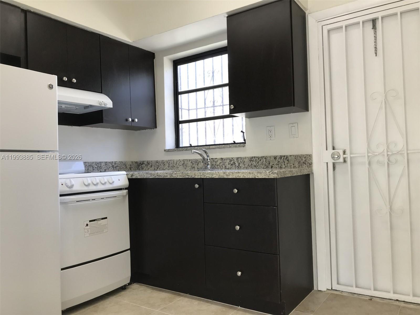 A kitchen features dark cabinets, granite countertops, a white stove, and a white security door — 2362 NW 34th St # 2, Miami FL 33142, MIAMI, FL