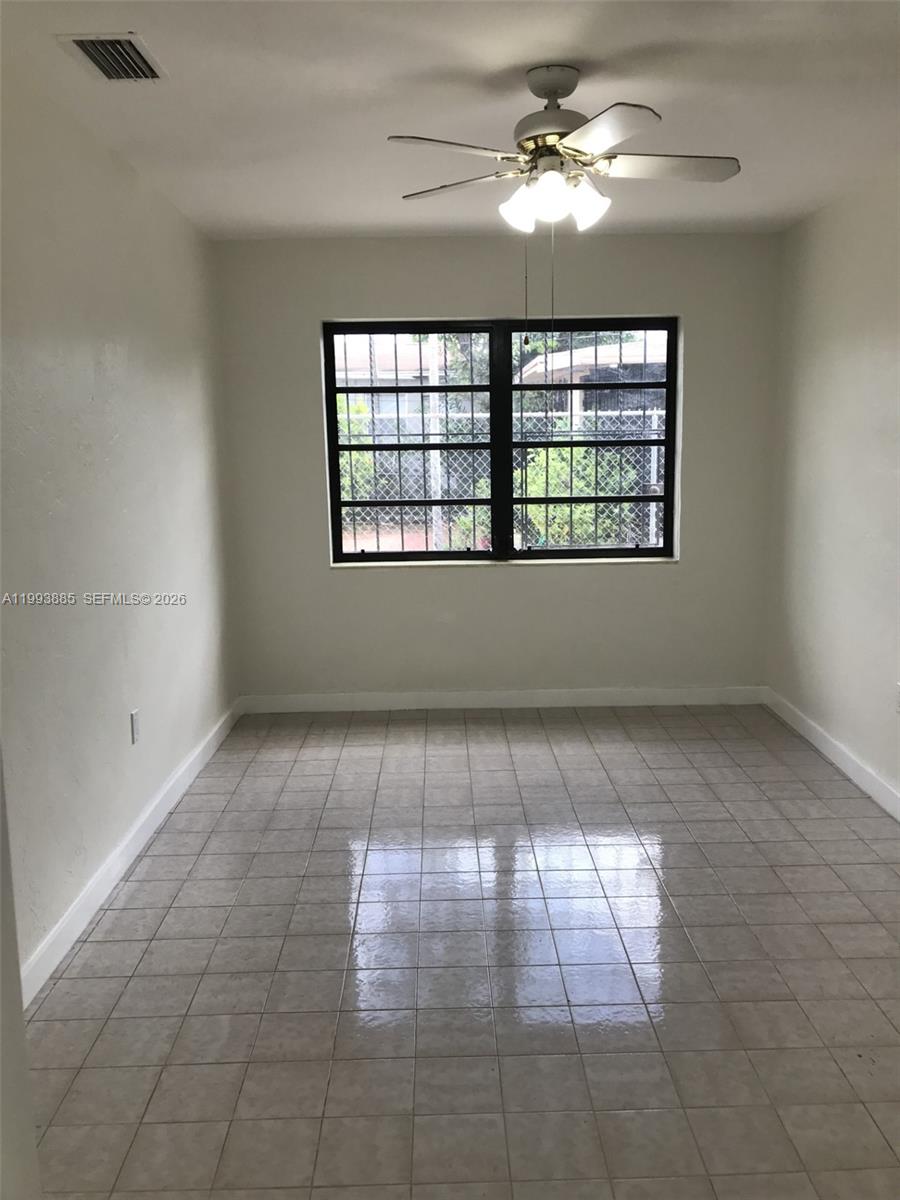 An empty room features light-colored tile flooring, white walls, a ceiling fan, and barred windows — 2362 NW 34th St # 2, Miami FL 33142, MIAMI, FL