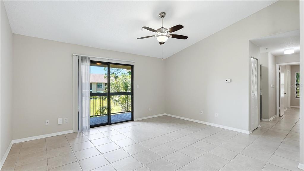 An empty living room with light tile flooring, a ceiling fan, and sliding glass balcony doors — 4033 CROCKERS LAKE BOULEVARD UNIT 28, SARASOTA, FL