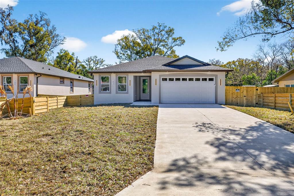 A single-story house with a white garage, concrete driveway, and wooden fence on a sunny day — 284 ROOSEVELT AVENUE, MASARYKTOWN, FL