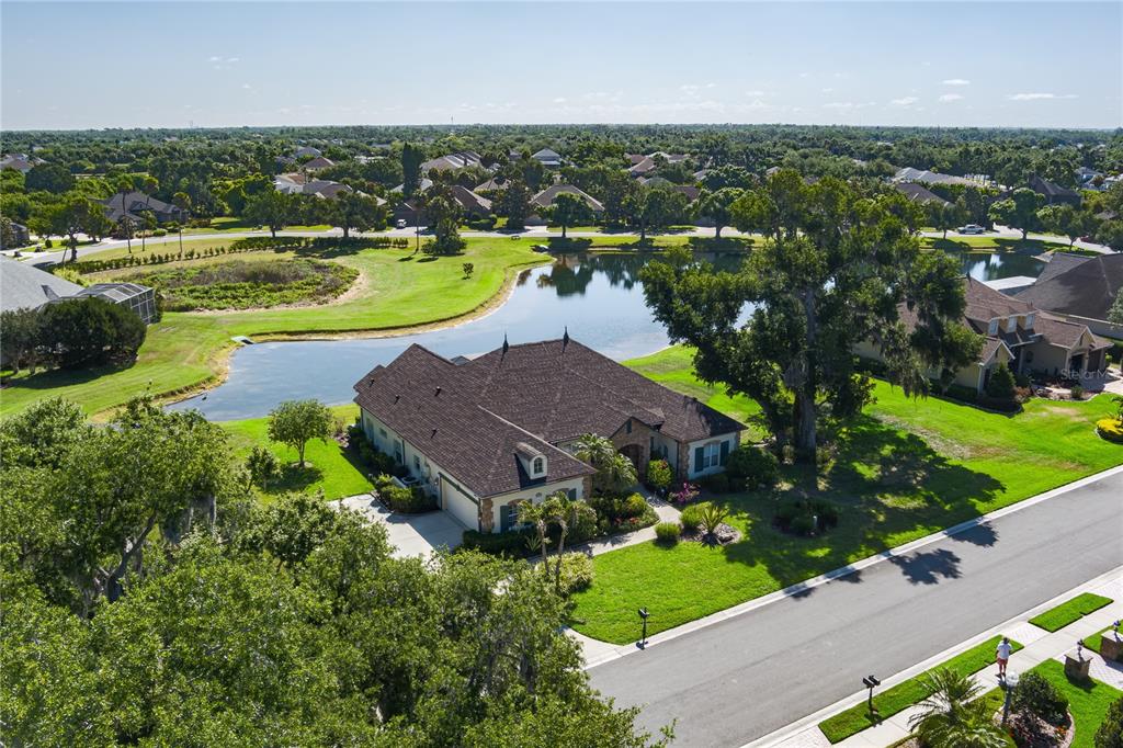 An aerial view shows a single-story house with a dark roof beside a pond — 3720 59TH AVENUE CIRCLE E, ELLENTON, FL