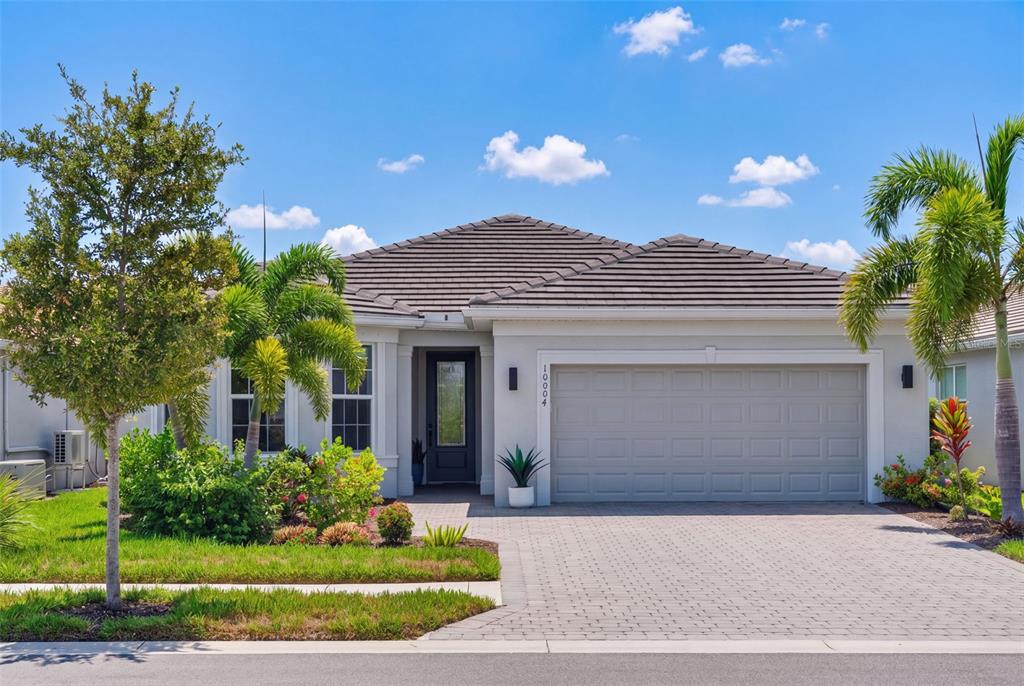 A single-story house with a gray tiled roof, a two-car garage, and a paved driveway — 10004 CORAL SHORE DRIVE, ENGLEWOOD, FL