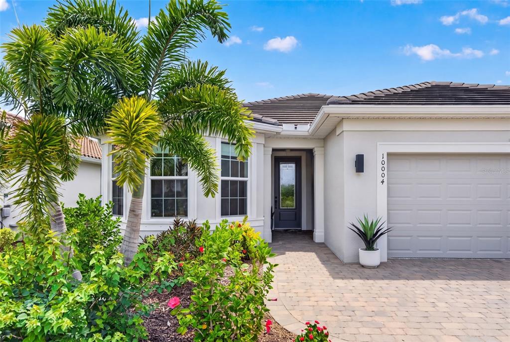 A single-story house exterior features a paved driveway, a gray garage door, and palm trees — 10004 CORAL SHORE DRIVE, ENGLEWOOD, FL