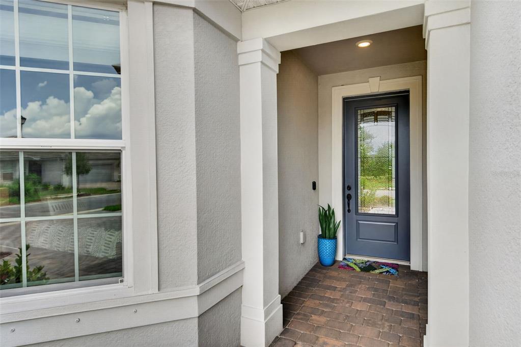 A gray front door with a glass insert sits under a covered entryway with pavers — 10004 CORAL SHORE DRIVE, ENGLEWOOD, FL
