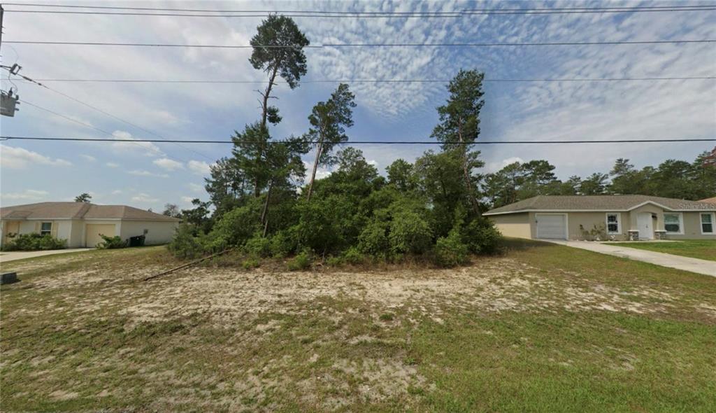 A vacant, wooded residential lot sits between two single-story houses under a cloudy sky — TBD MARION OAKS MNR, OCALA, FL