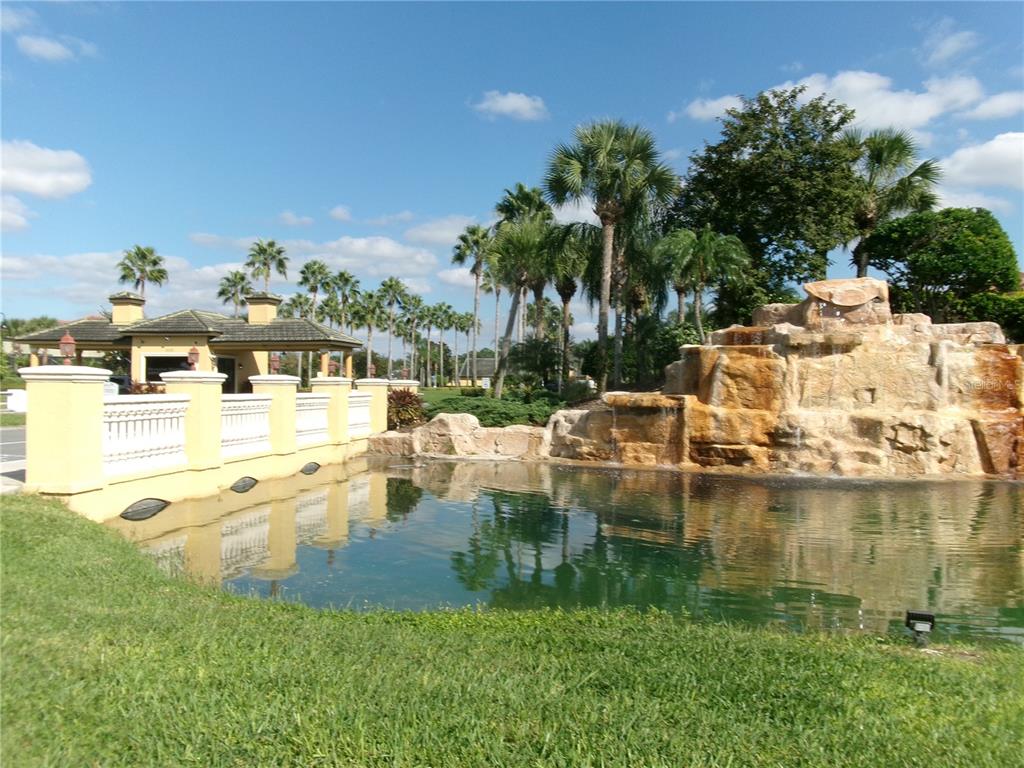 A stone waterfall feature sits beside a pond and a decorative wall near palm trees — 8969 MAJESTY PALM ROAD, KISSIMMEE, FL