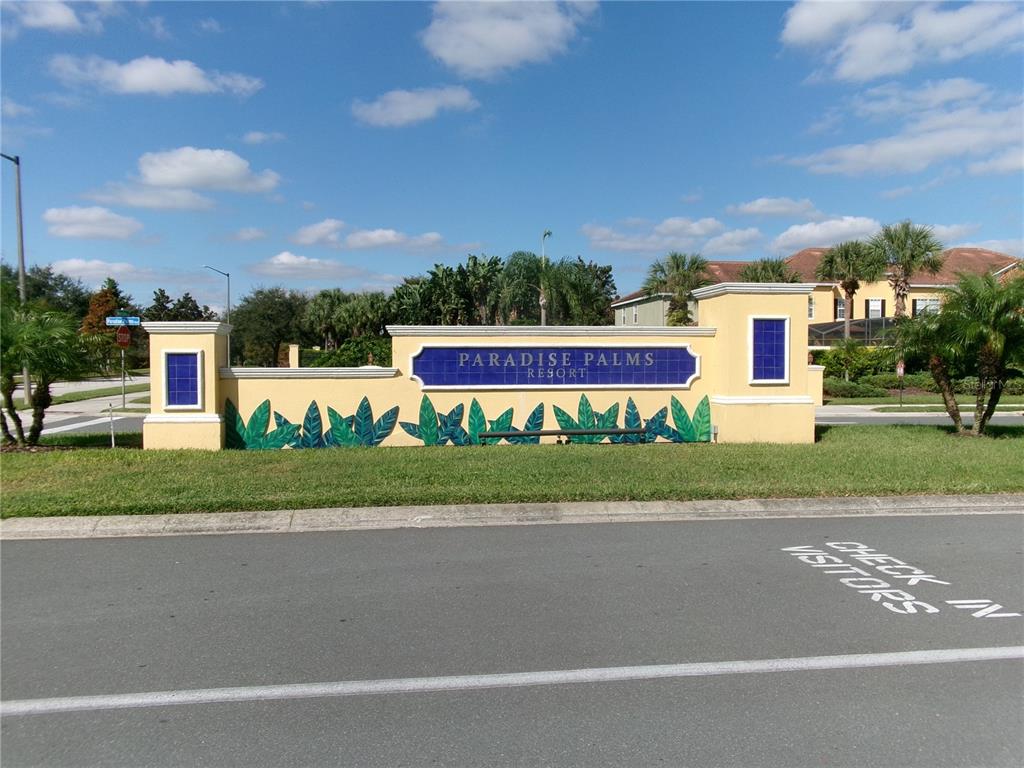 A beige stucco monument sign for Paradise Palms Resort sits beside a paved road — 8969 MAJESTY PALM ROAD, KISSIMMEE, FL