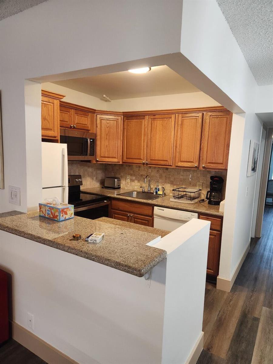A kitchen features wood cabinets, granite countertops, and a breakfast bar overlooking the living area — 102 E Westbury # 102, Deerfield Beach FL 33442, DEERFIELD BEACH, FL