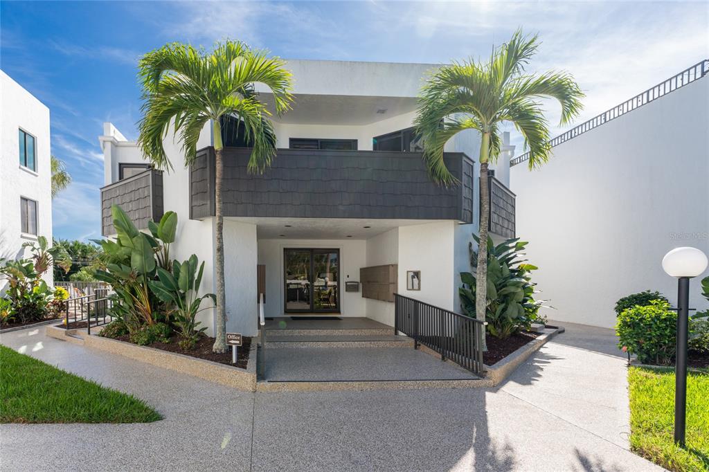 The exterior of a two-story building features a covered entrance, palm trees, and landscaping — 2955 N BEACH ROAD UNIT E122, ENGLEWOOD, FL