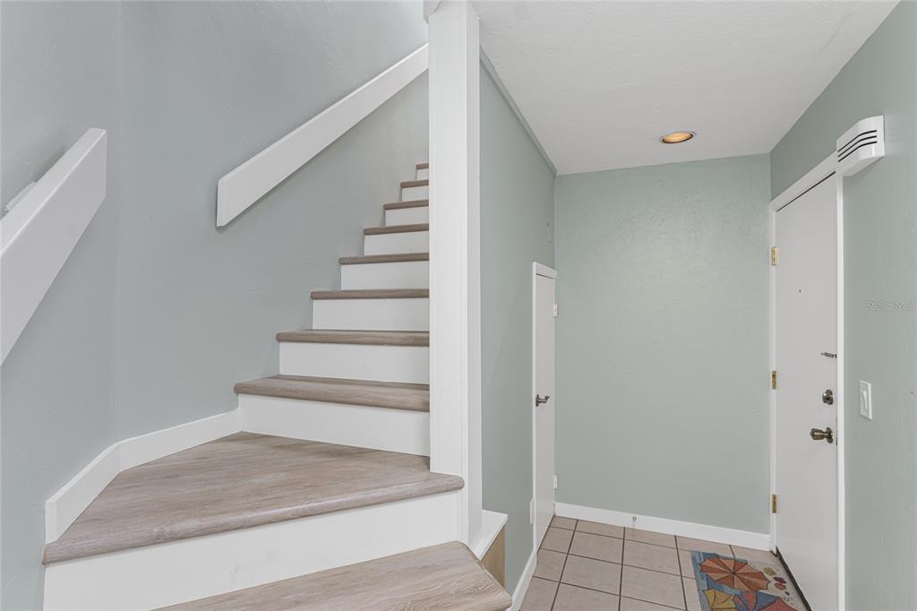 An entryway features a staircase with wood-look treads, light green walls, and tiled flooring — 2955 N BEACH ROAD UNIT E122, ENGLEWOOD, FL