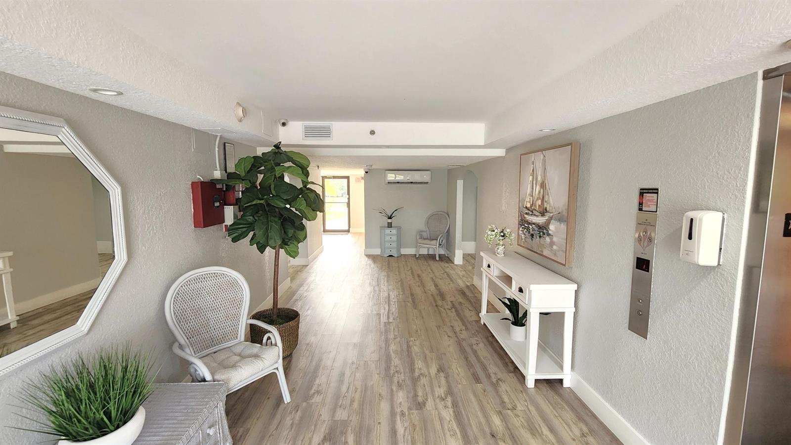 A bright hallway features light wood-look flooring, white furniture, a large potted plant, and an elevator — 2455 Lindell Boulevard # 3511, Delray Beach FL 33444, DELRAY BEACH, FL