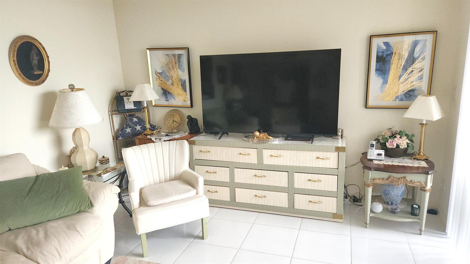 A living room features a large television on a dresser, an armchair, and two lamps — 2455 Lindell Boulevard # 3511, Delray Beach FL 33444, DELRAY BEACH, FL