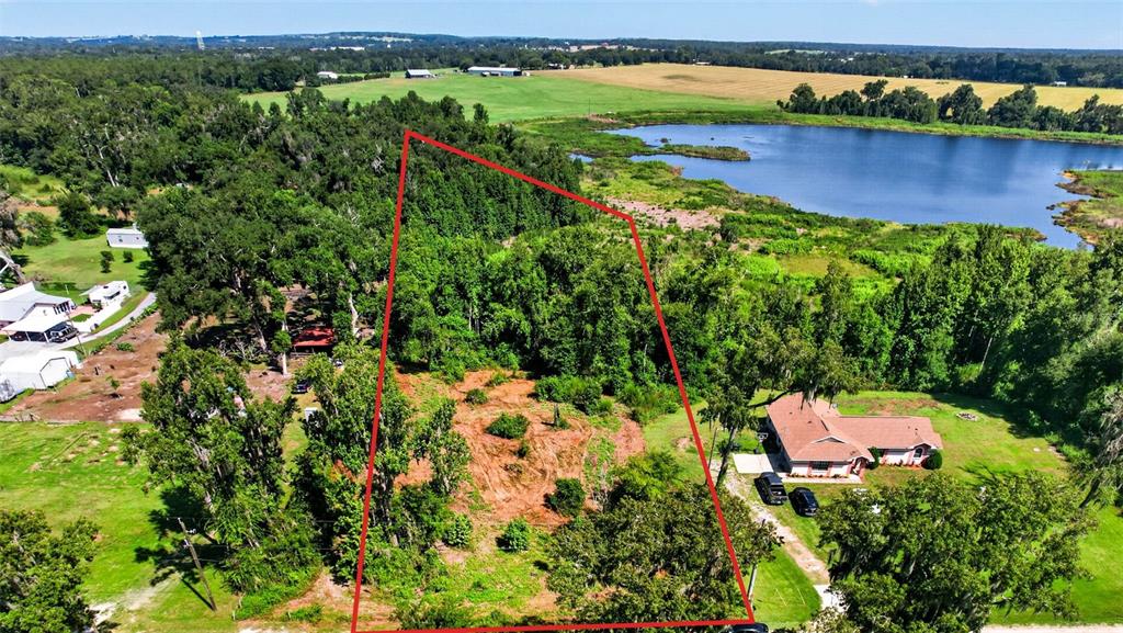 An aerial view shows a wooded lot outlined in red next to a house and lake — 0 SUMNER LAKE ROAD, DADE CITY, FL