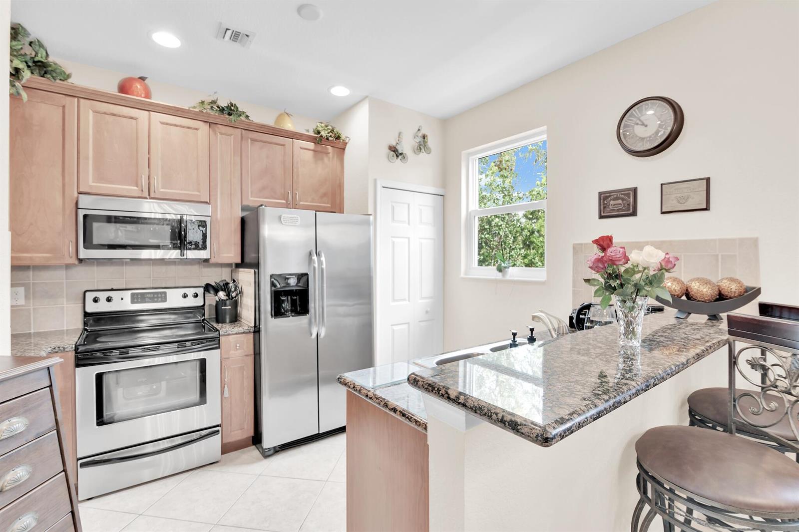 A kitchen features light wood cabinets, stainless steel appliances, and a granite-topped breakfast bar — 528 Bayfront Drive, Boynton Beach FL 33435, BOYNTON BEACH, FL