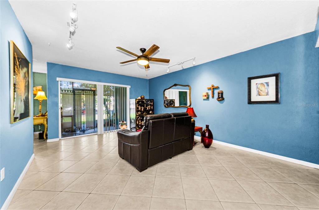 A living room features blue walls, tile flooring, a ceiling fan, and a sliding glass door — 11436 2ND STREET N UNIT 1, ST PETERSBURG, FL