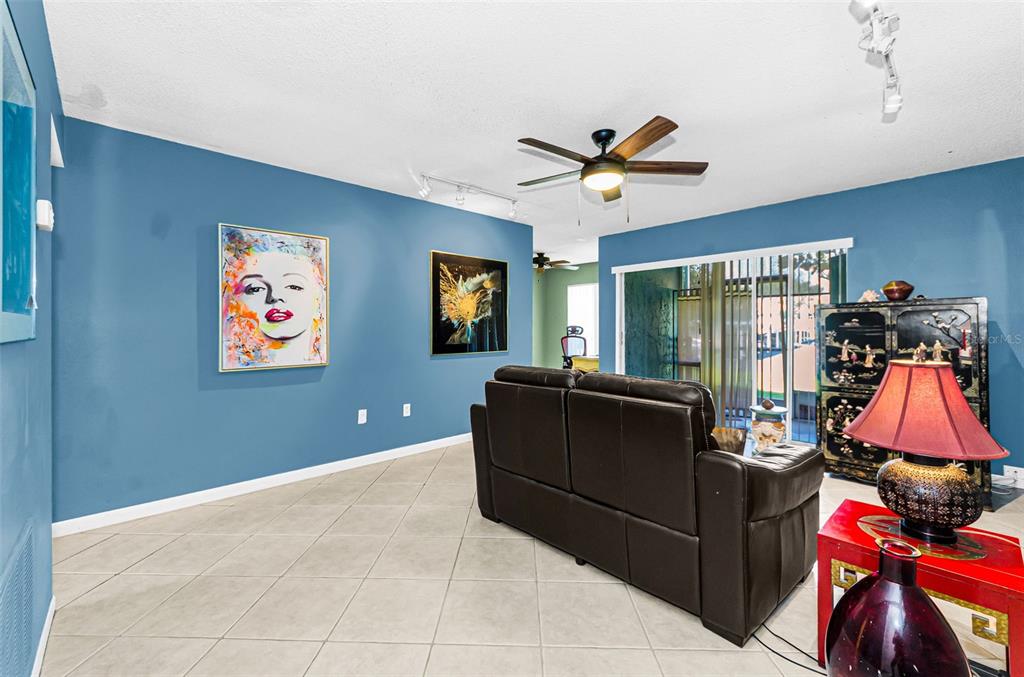 A living room features blue walls, a dark leather sofa, tile flooring, and a ceiling fan — 11436 2ND STREET N UNIT 1, ST PETERSBURG, FL