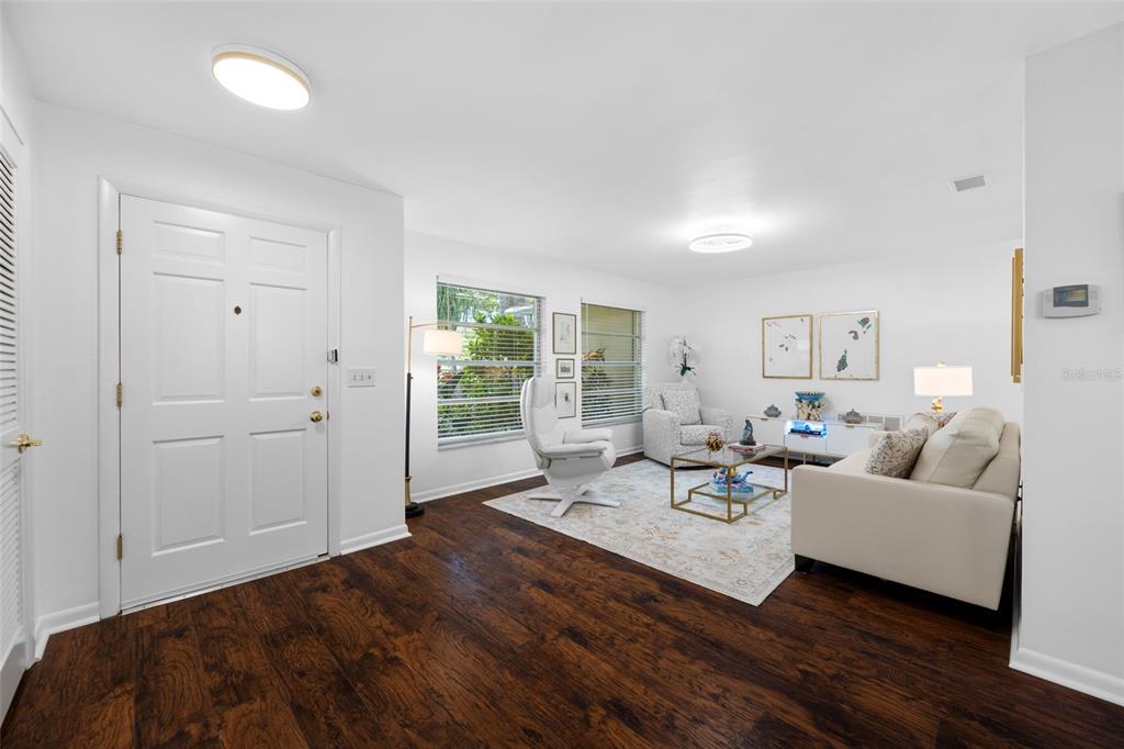 A bright living room features dark wood flooring, white walls, and a white sofa — 2036 FOREST DRIVE, CLEARWATER, FL