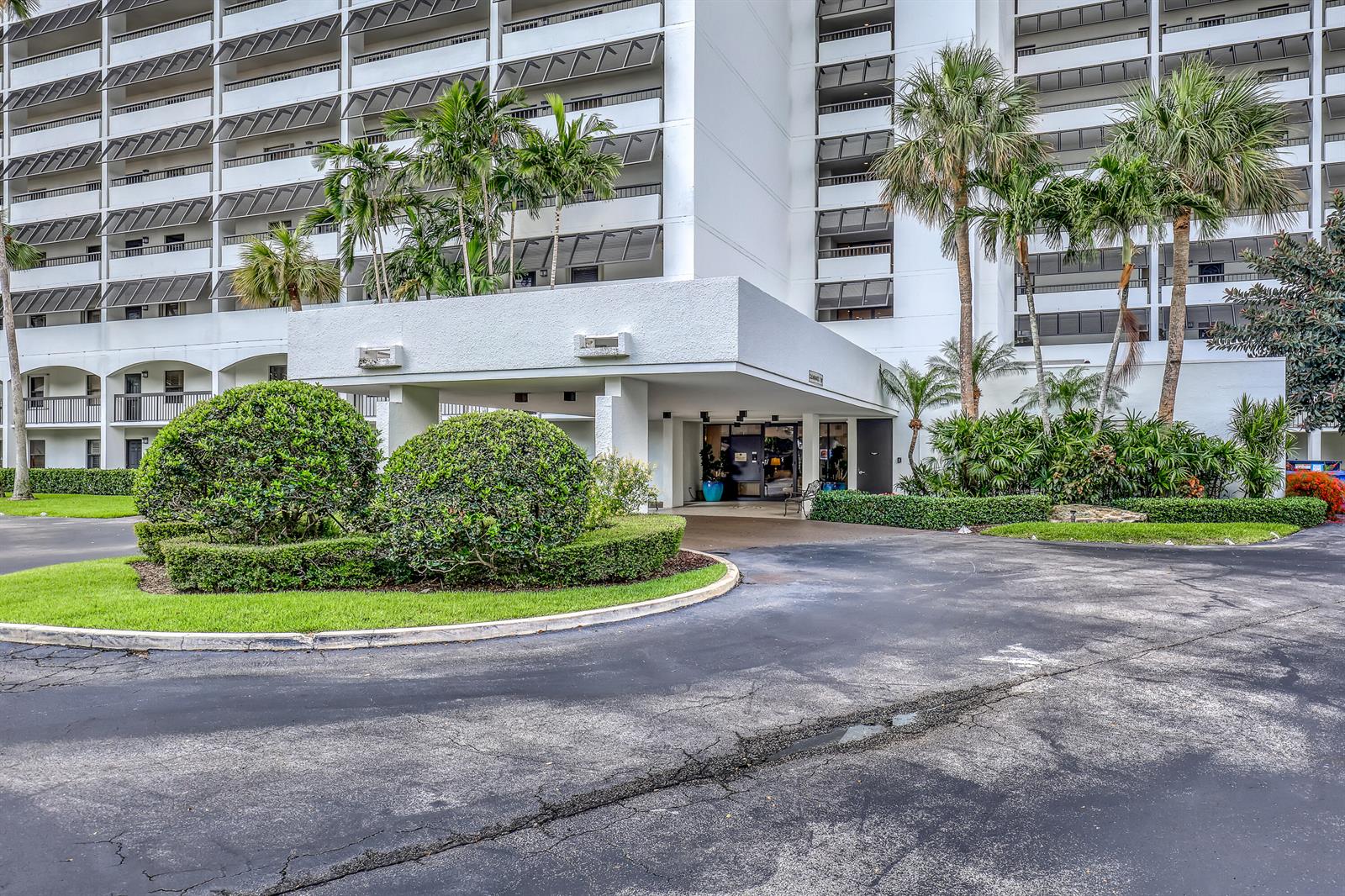The exterior of a multi-story white apartment building features a covered entrance and landscaping — 356 Golfview Road # 403, North Palm Beach FL 33408, NORTH PALM BEACH, FL