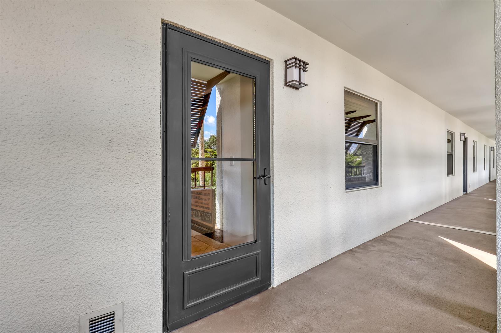 A gray storm door leads to a covered outdoor walkway with white stucco walls — 356 Golfview Road # 403, North Palm Beach FL 33408, NORTH PALM BEACH, FL