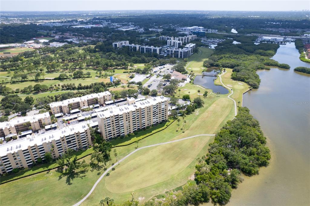 An aerial view shows multi-story apartment buildings situated next to a golf course and water — 2618 COVE CAY DRIVE UNIT 702, CLEARWATER, FL