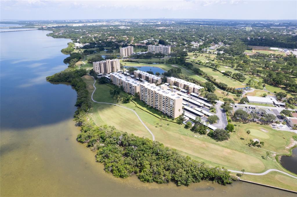 An aerial view of waterfront apartment buildings situated next to a golf course and trees — 2618 COVE CAY DRIVE UNIT 702, CLEARWATER, FL