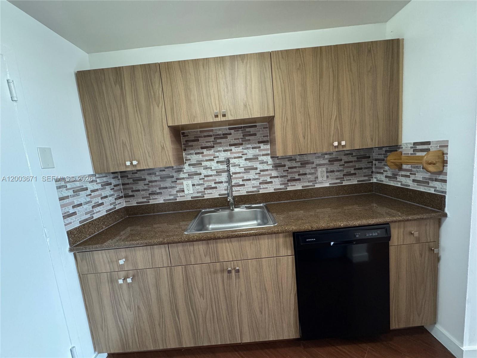 A kitchen features wood-grain cabinets, a brown granite countertop, and a mosaic tile backsplash — 2020 NE 135th St # 810, North Miami FL 33181, NORTH MIAMI, FL