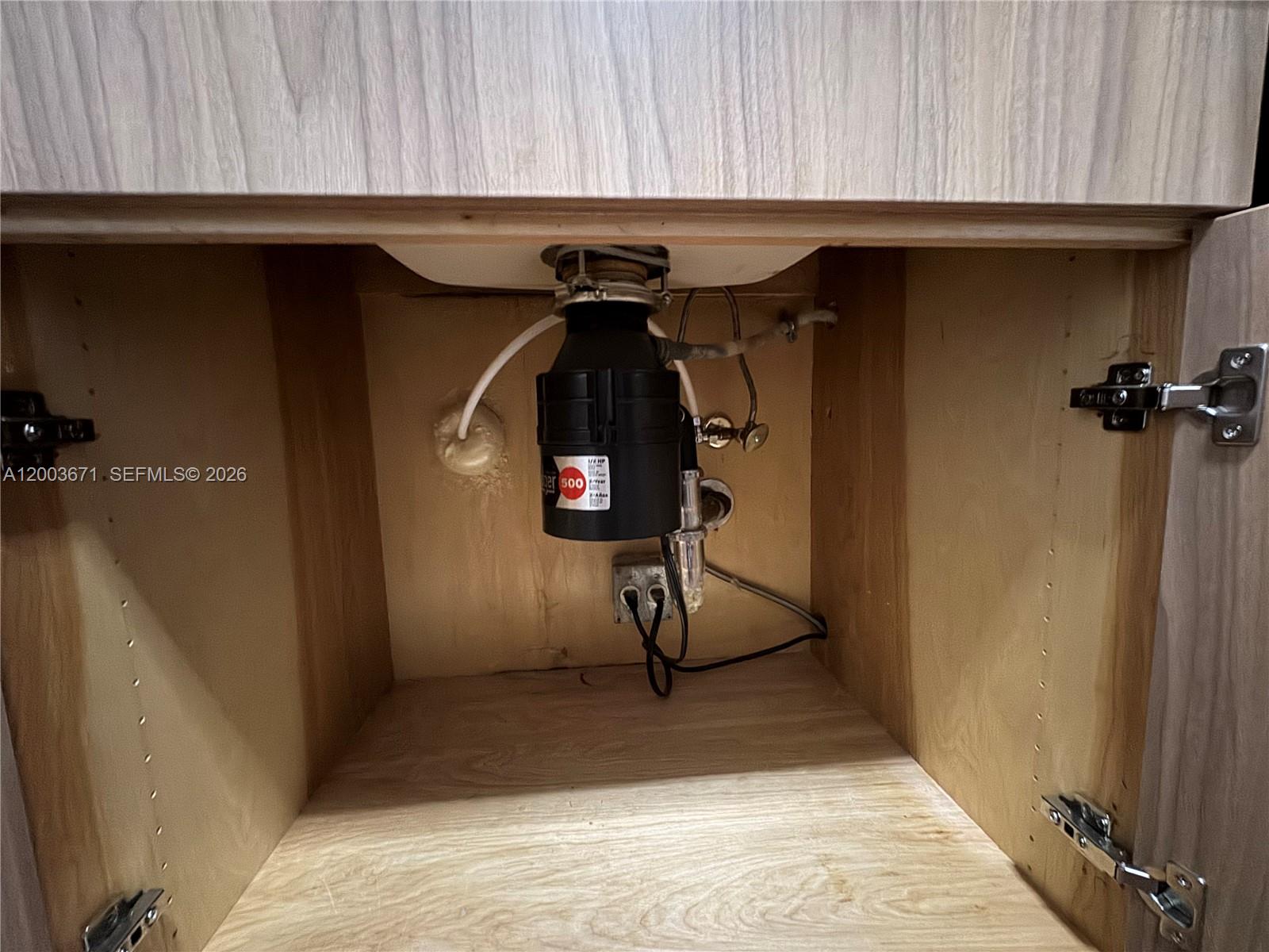 This image shows the interior of a kitchen sink cabinet featuring a garbage disposal unit — 2020 NE 135th St # 810, North Miami FL 33181, NORTH MIAMI, FL