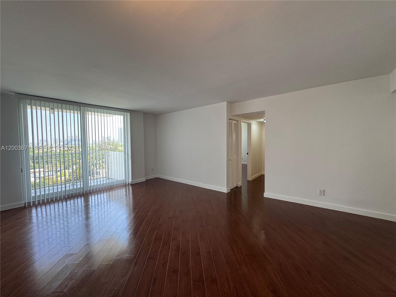 An empty room features dark wood flooring, white walls, and a large sliding glass door — 2020 NE 135th St # 810, North Miami FL 33181, NORTH MIAMI, FL