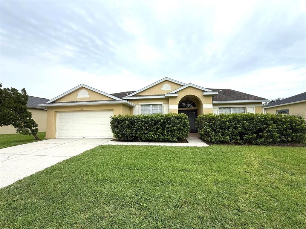 A single-story house with a two-car garage, a front lawn, and a large hedge — 5335 BOLD VENTURE PLACE, WESLEY CHAPEL, FL