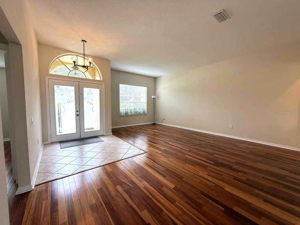 An empty living room features wood flooring, a tiled entryway, and double front doors — 5335 BOLD VENTURE PLACE, WESLEY CHAPEL, FL