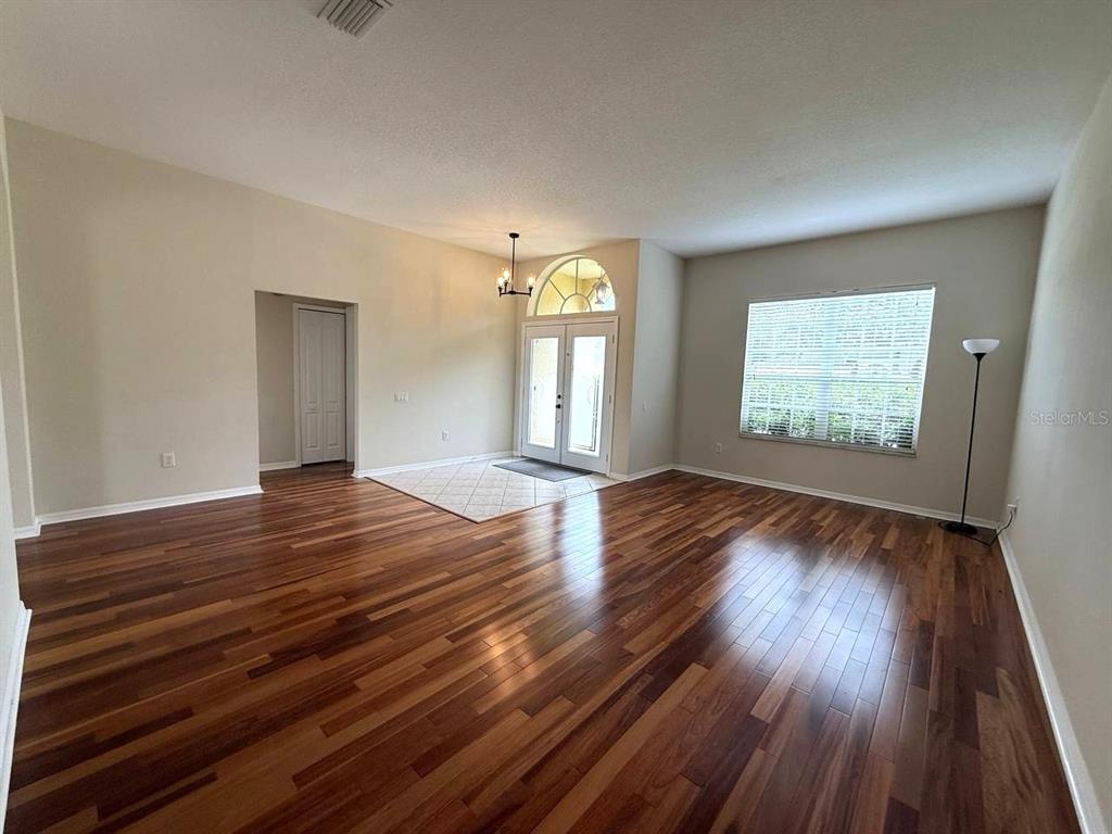 An empty living room features dark wood flooring, a tiled entryway, and a front door — 5335 BOLD VENTURE PLACE, WESLEY CHAPEL, FL