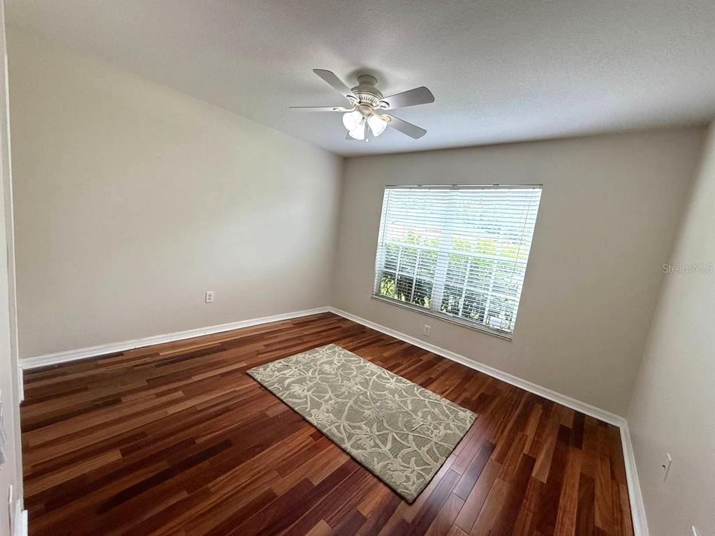 An empty bedroom features hardwood flooring, a ceiling fan, and a window with blinds — 5335 BOLD VENTURE PLACE, WESLEY CHAPEL, FL