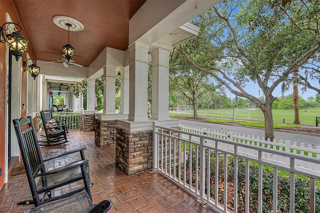 A covered front porch features rocking chairs, stone-based columns, and a view of a park — 3614 WIREGRASS ROAD, NEW PORT RICHEY, FL