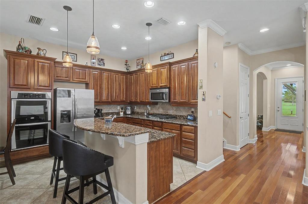 A kitchen features wood cabinets, granite countertops, stainless steel appliances, and a breakfast bar — 3614 WIREGRASS ROAD, NEW PORT RICHEY, FL